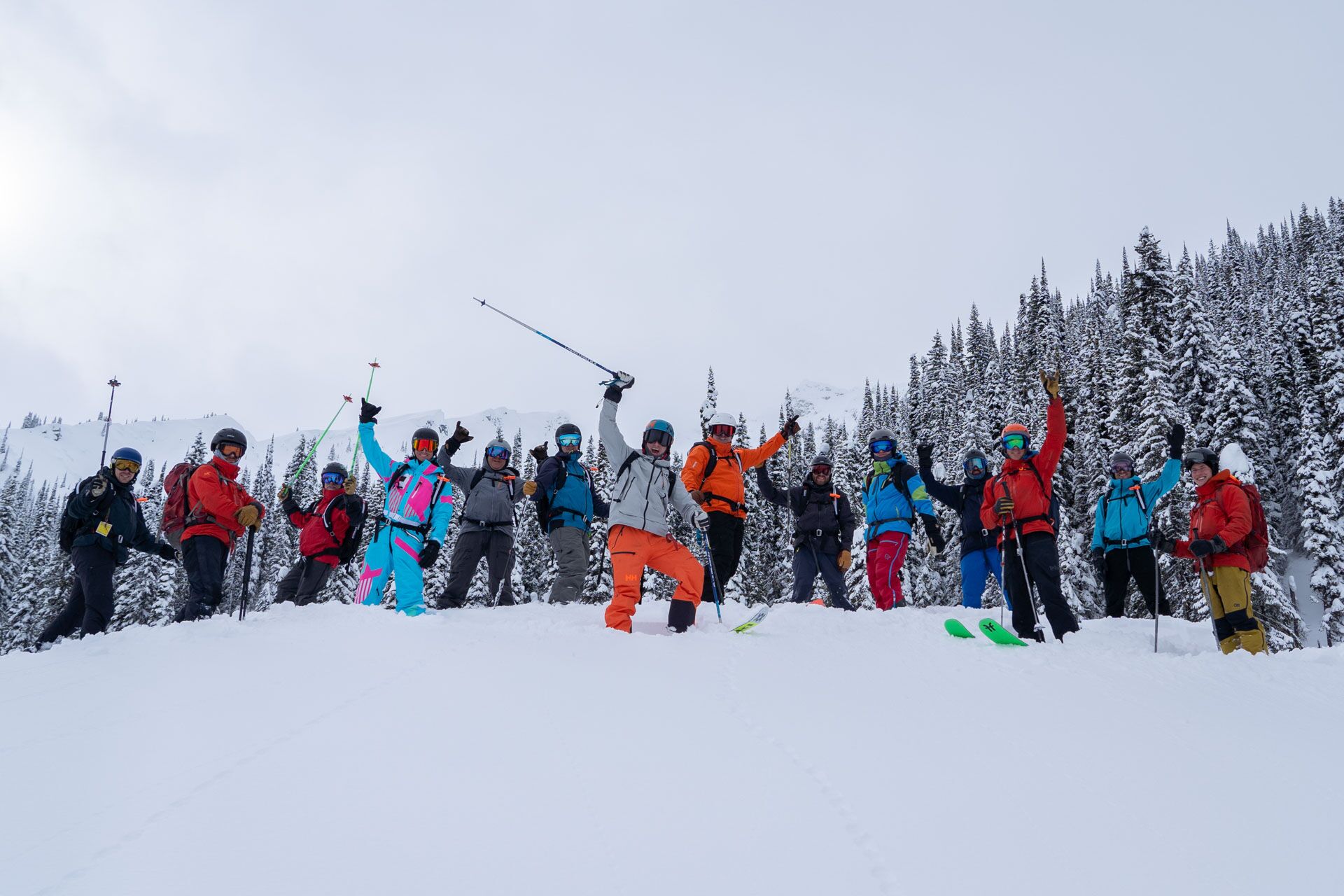 Group of skiers in vibrant jackets striking a triumphant pose with arms raised at White Grizzly Cat Skiing.